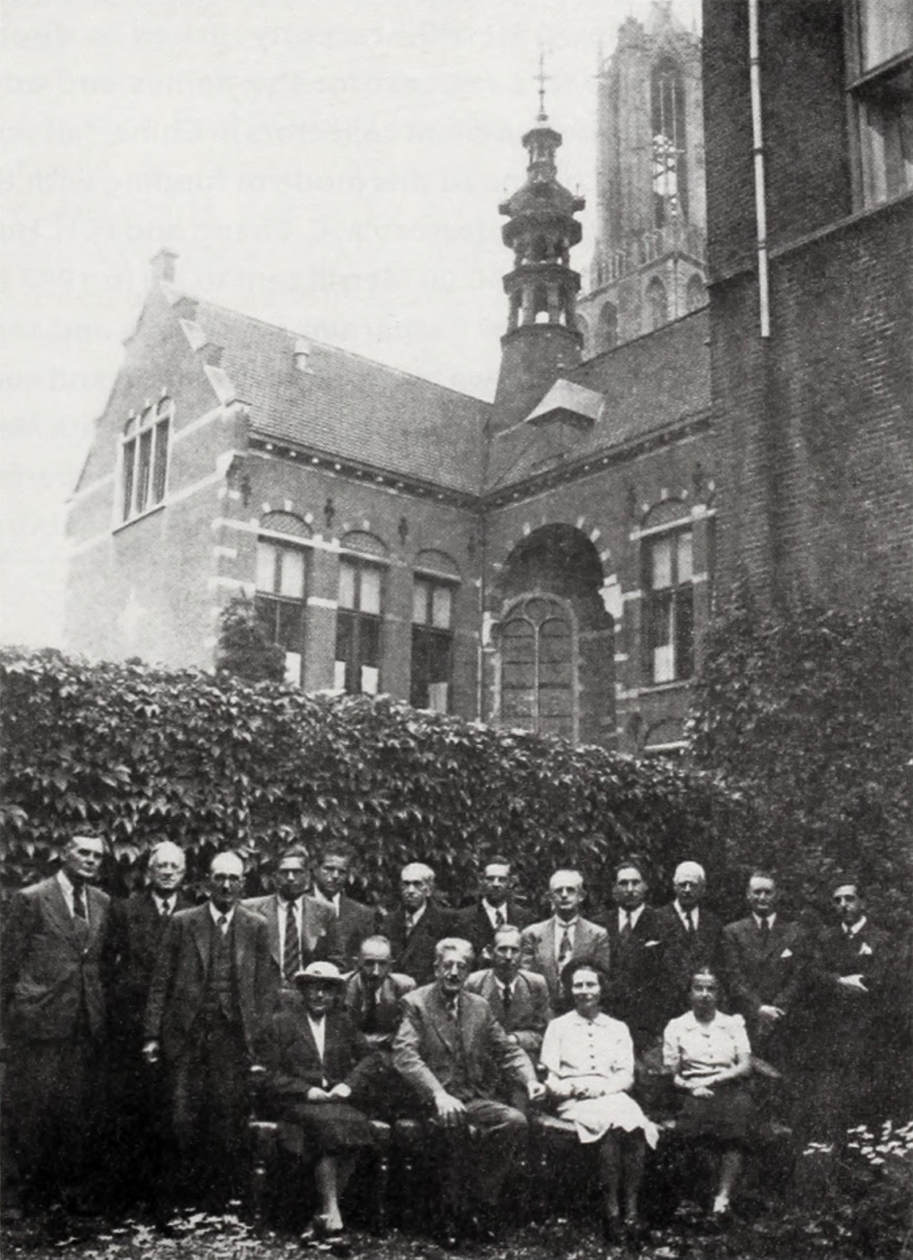 Black-and-white photograph of group standing in front of large building