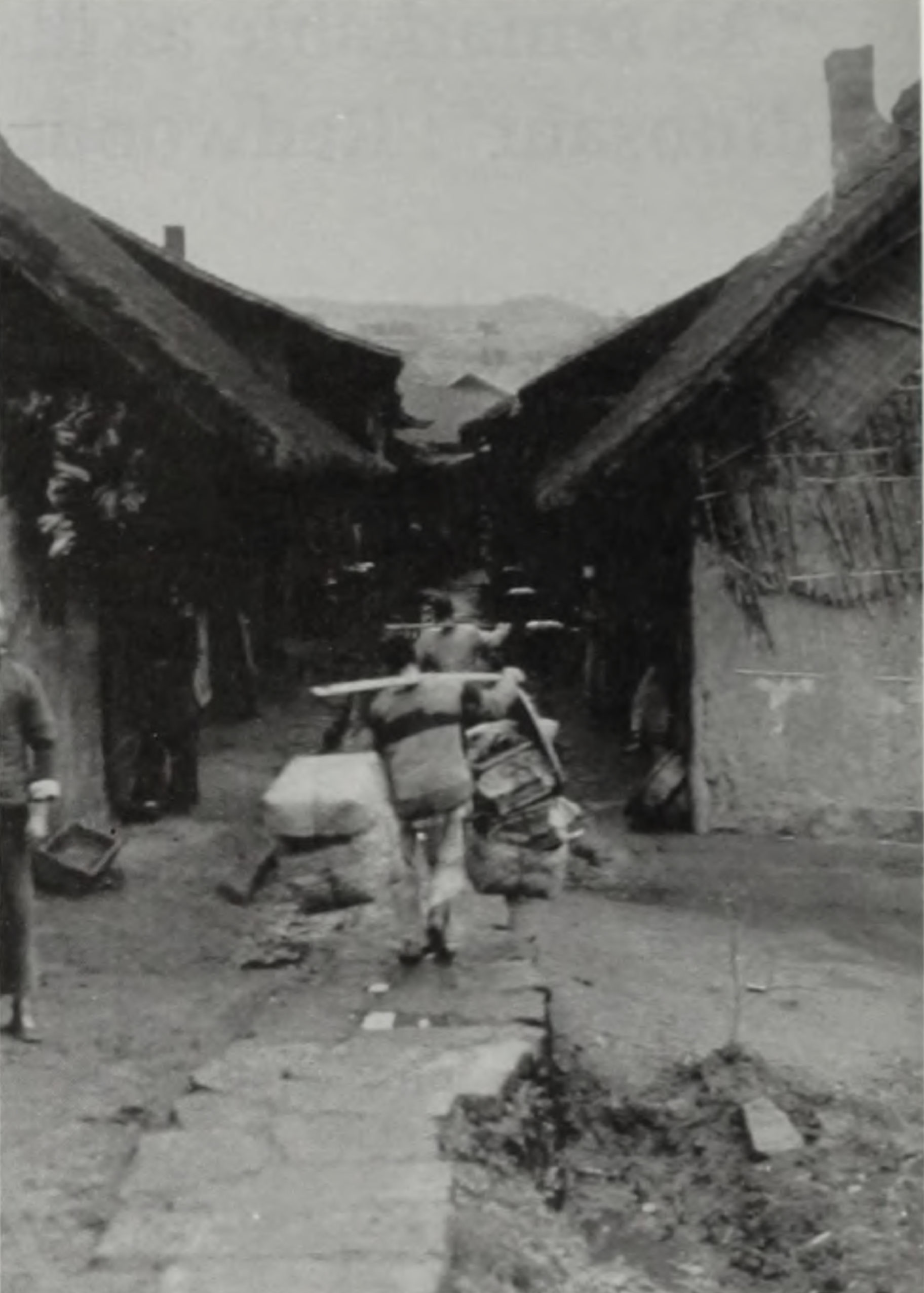 Black-and-white landscape image showing men carrying packages