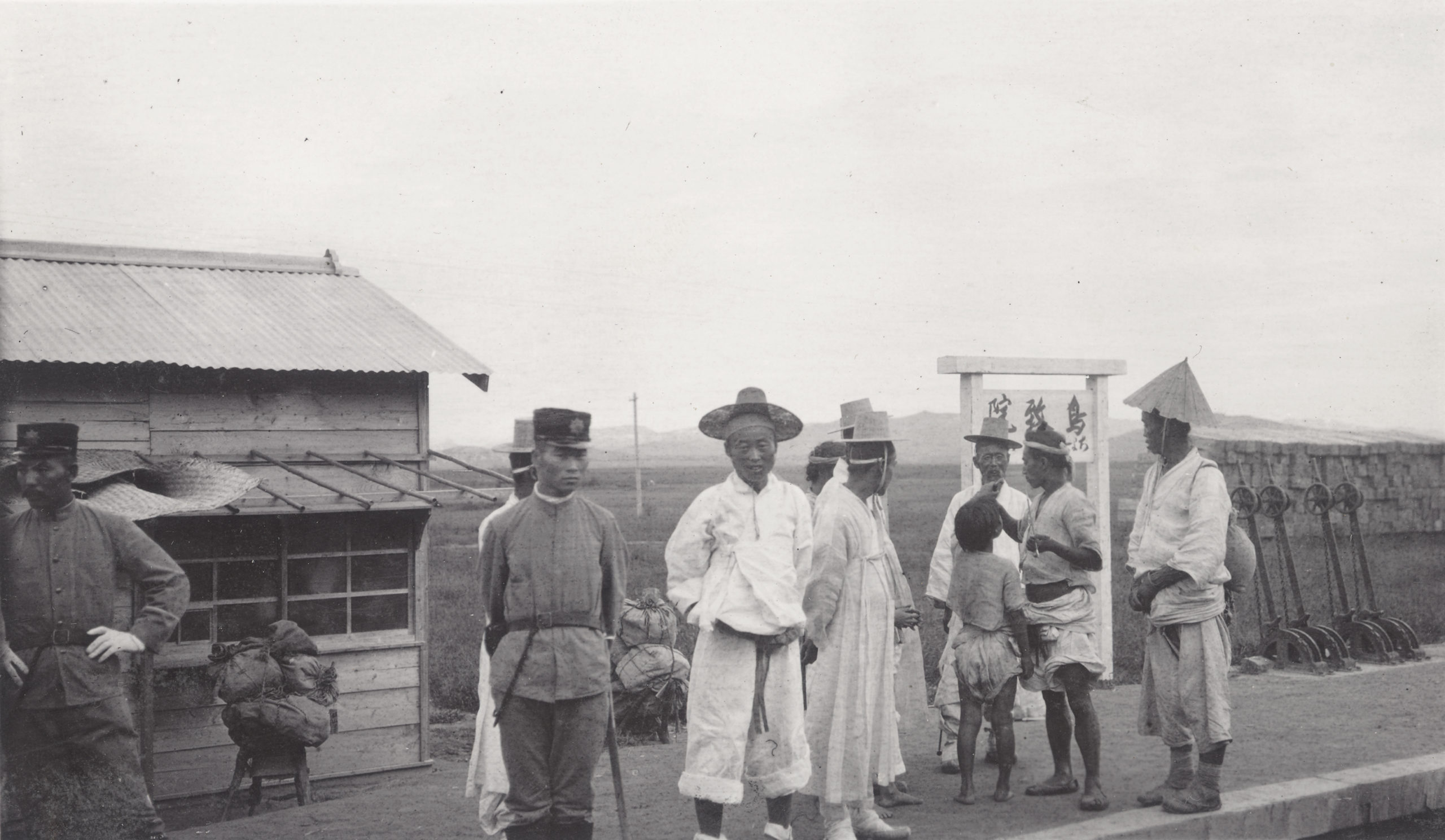 Koreans on the platform of a station on Seoul-Busan Railroad (Kei-Fu Railroad). Note the Japanese guards of the occupation forces standing in the middle and left of the picture. Photograph by John Jack, September 15, 1905.