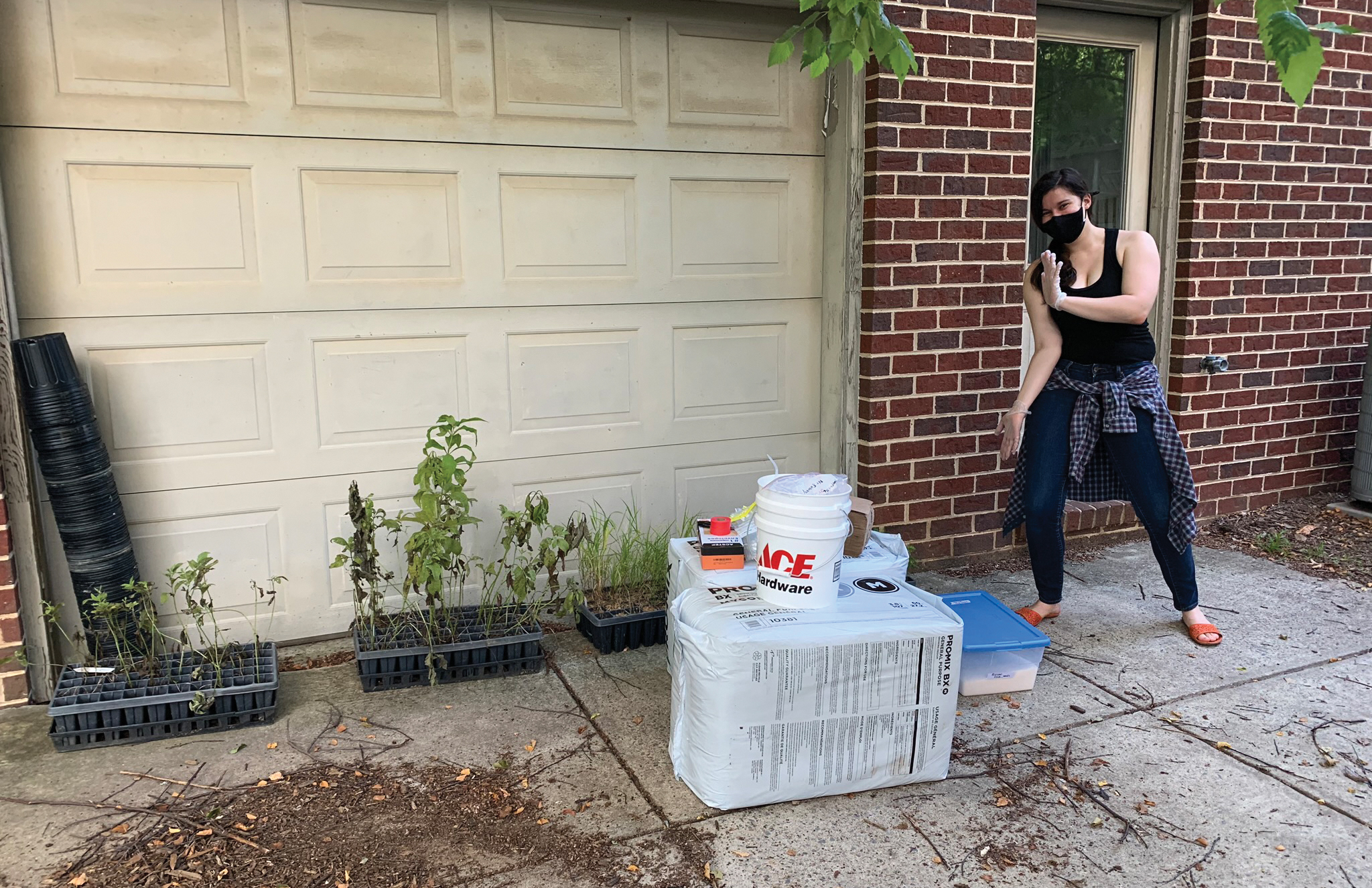 Photograph of researcher standing with plants, potting soil, and pots
