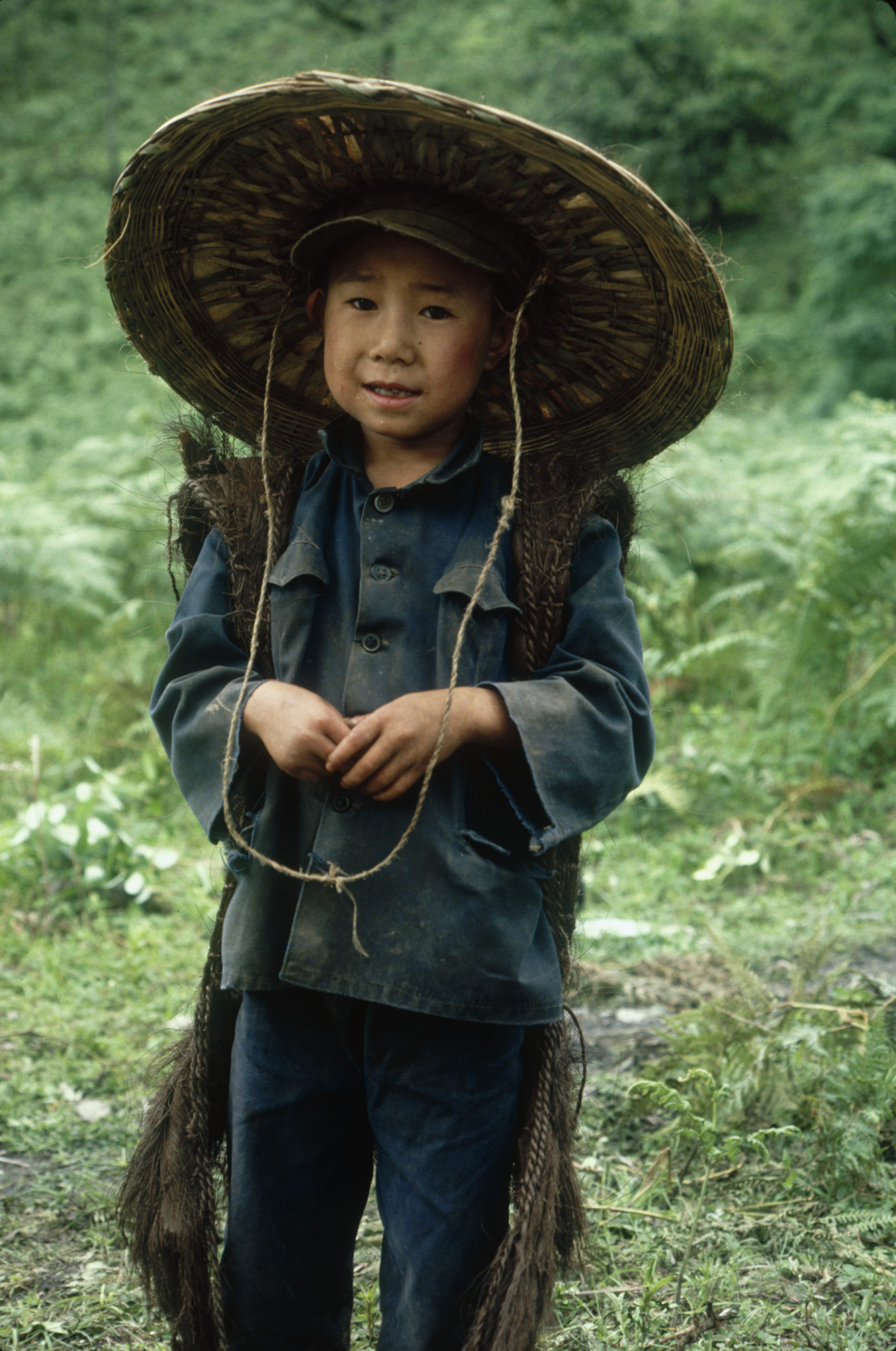 A young herder wearing a hat and a traditional raincoat made of fan palm Trachycarpus fibers in a meadow at Malutang, Yunnan.
