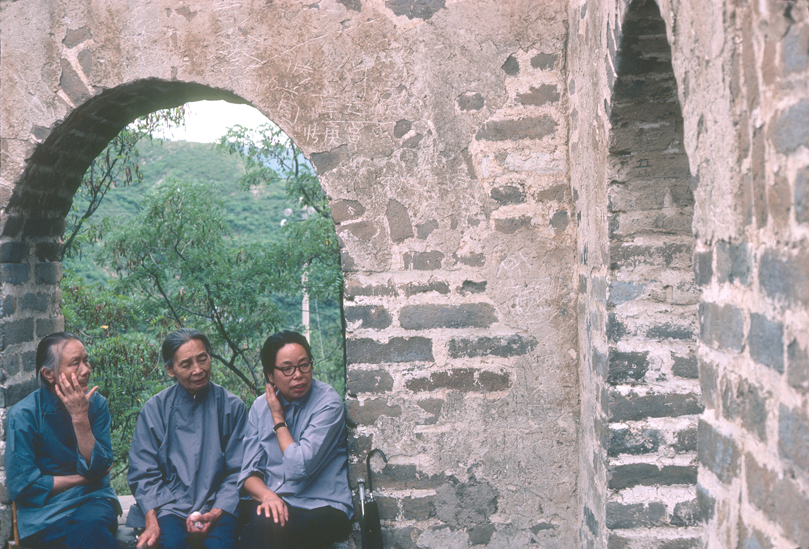 Three Chinese visitors pause to rest in a archway of the Great Wall.