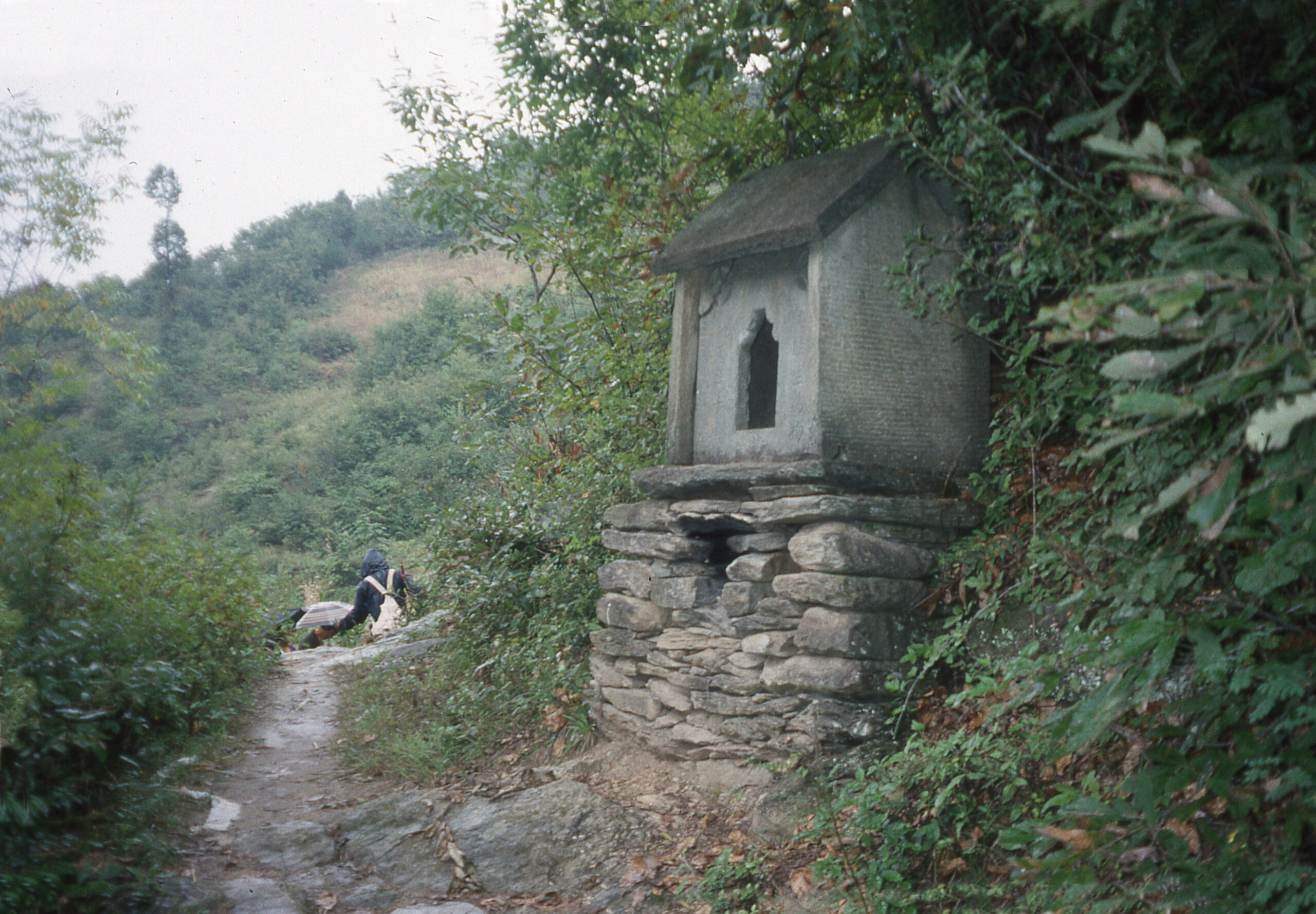 A small grey stone shire sit on top of a fieldstone base beside a path in Hubei, China.