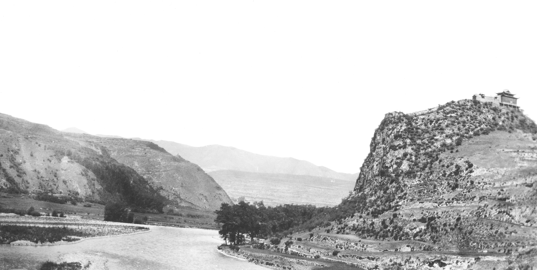 Black-and-white photograph of winding river with a temple perched on the hill above