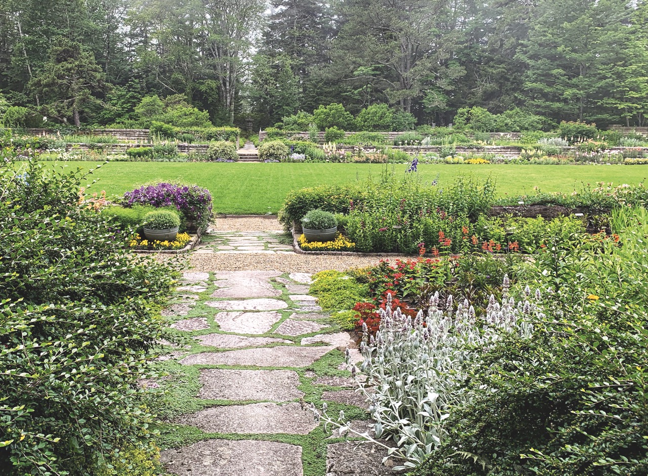 Stone garden path with planting beds, grass lawn, and mixed-conifer forest.