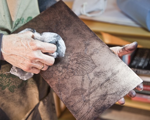 Artist's hand, holding cloth, rubbing ink from etched copper plate.