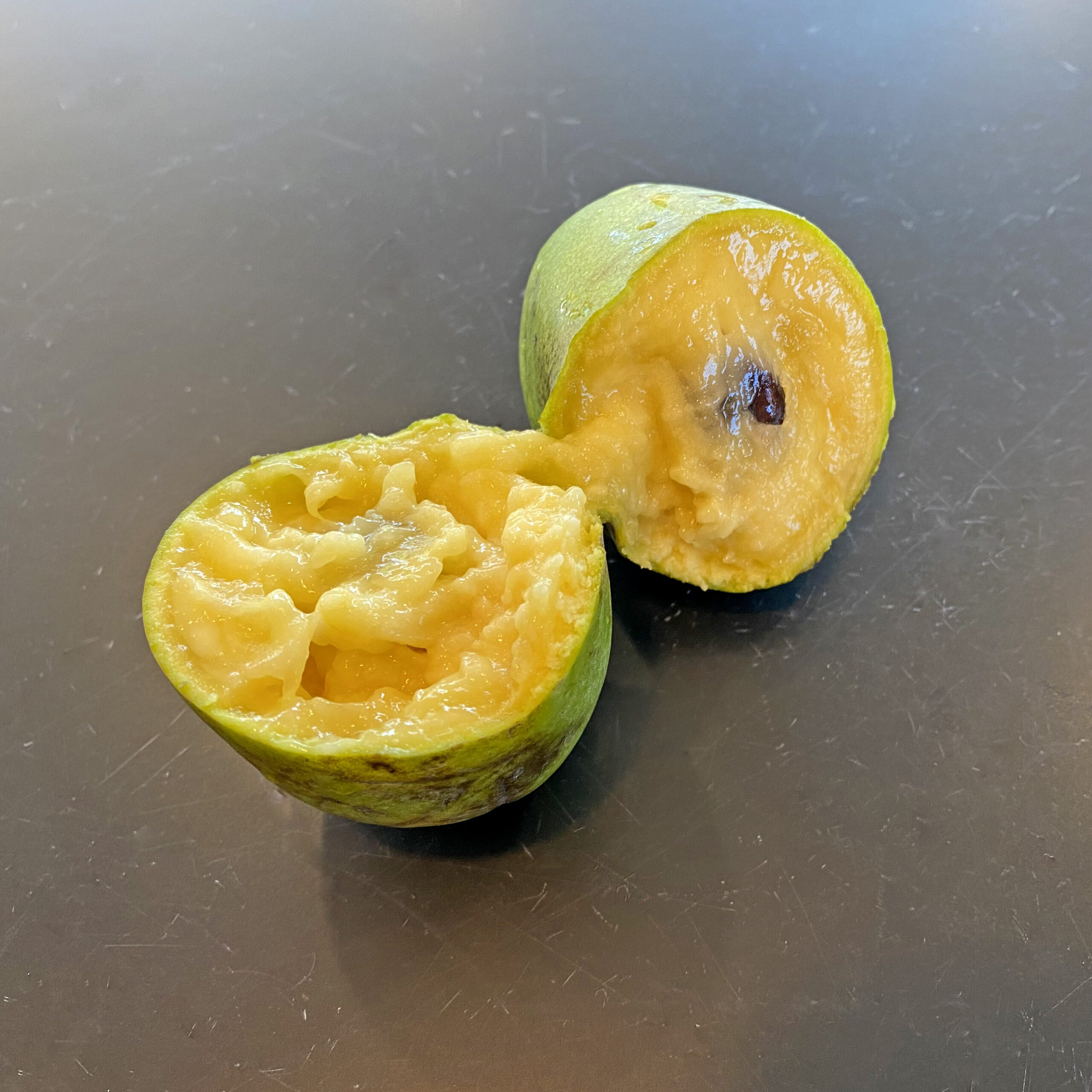 ripe fruit of paw paw, showing yellow flesh and one of the black seeds