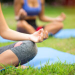 Two women do lotus pose on the grass